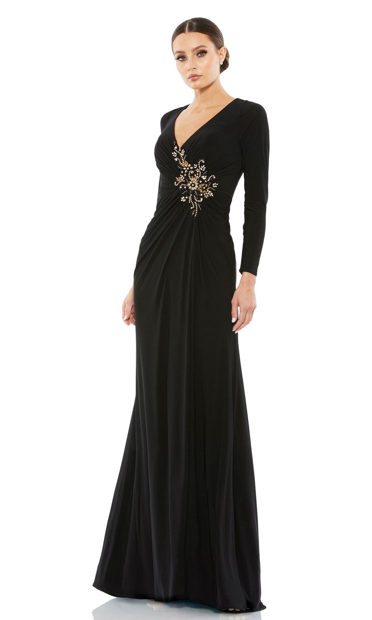 A woman wearing the Mac Duggal 67848 long sleeve formal dress with a V-neckline and gold floral waist embellishment stands against a white background.